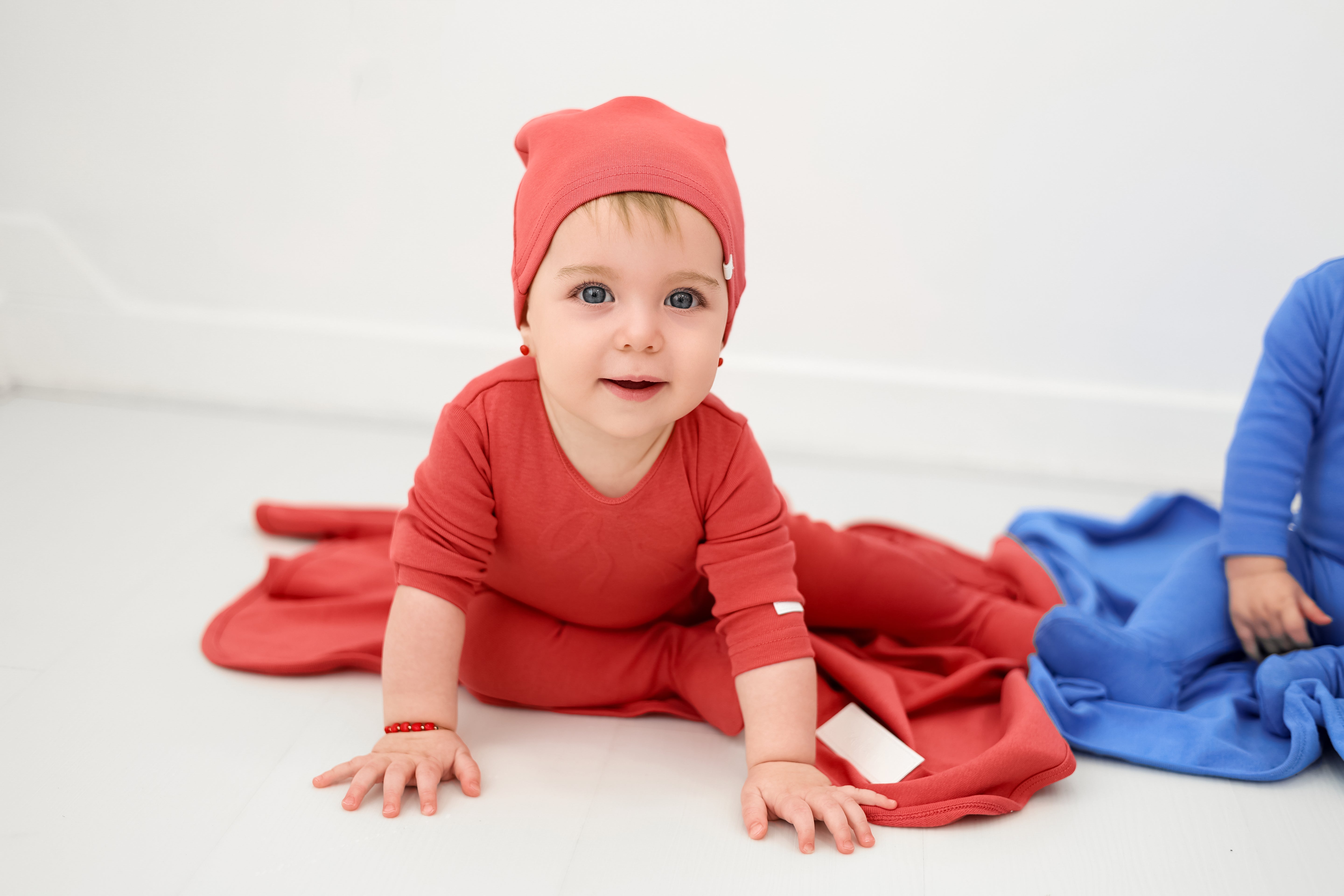 Baby in red outfit and hat sitting on a white surface