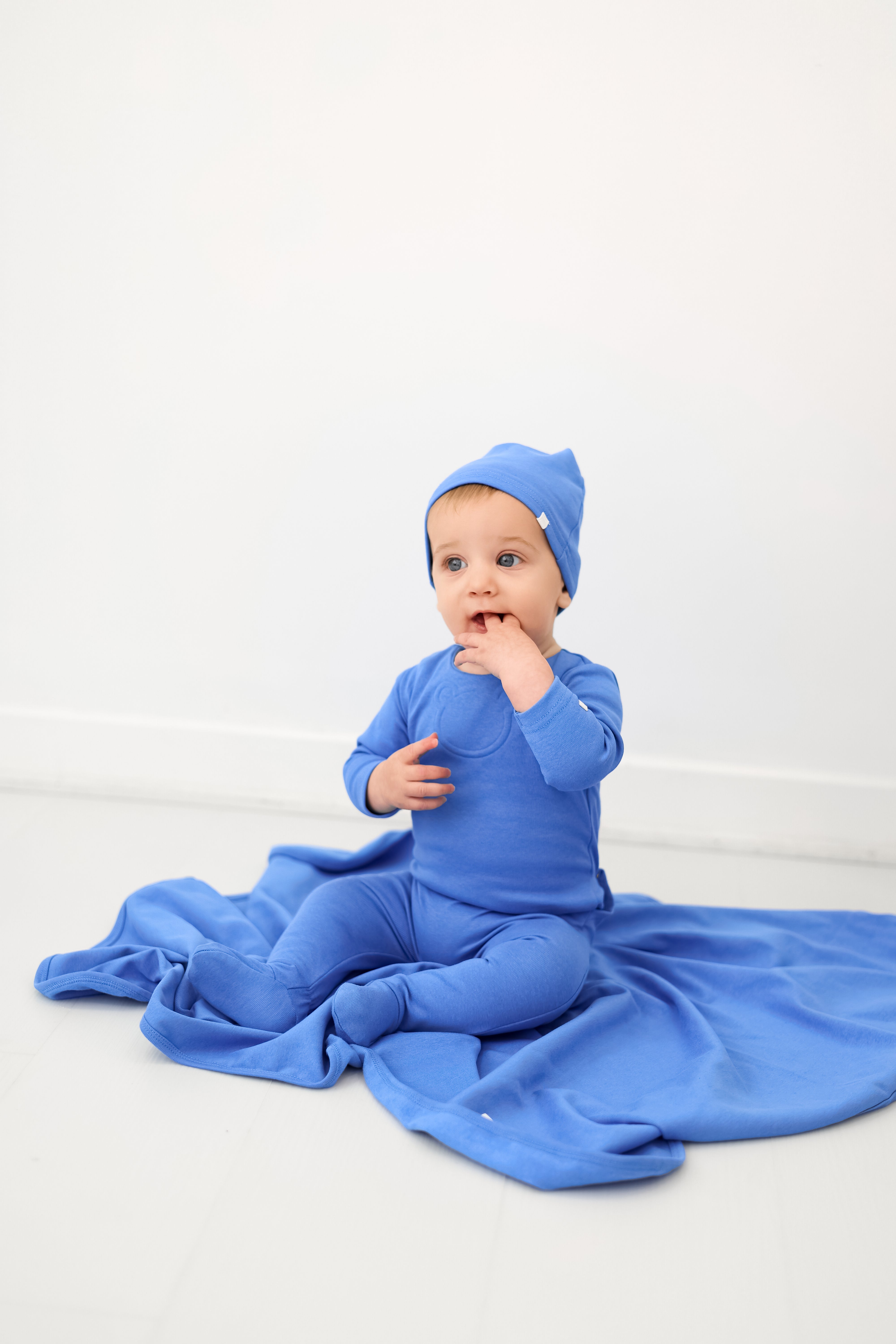 Baby in blue outfit and hat sitting on a white background