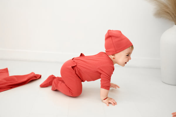 Baby in deep pink footie and hat crawling on a white surface